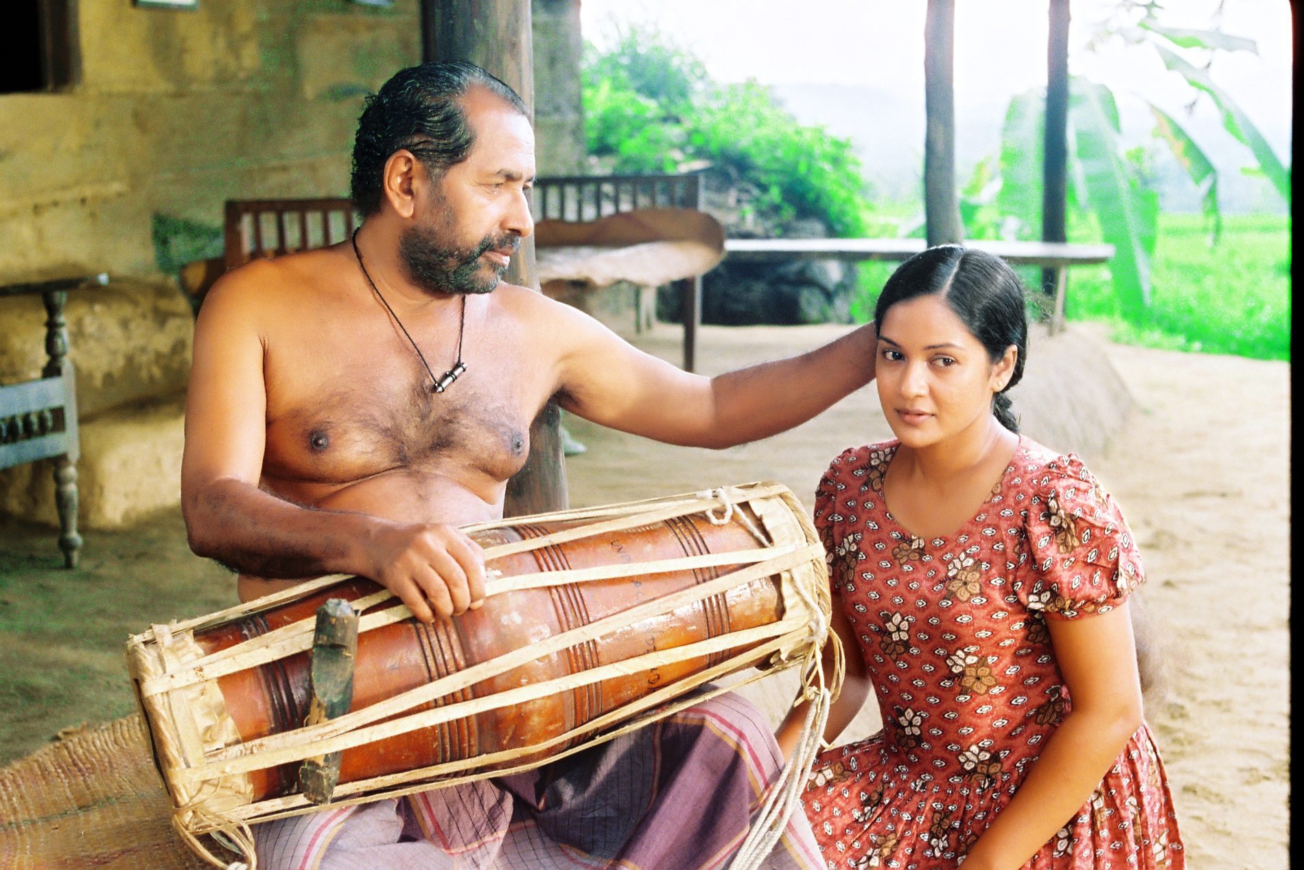 A drummer seated with his daughter on a veranda, a hand raised to her head.